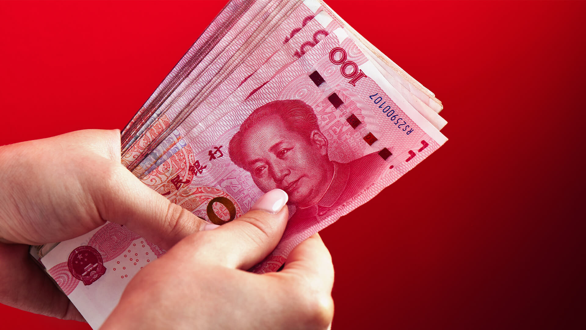 A pile of RMB banknotes of Chinese yuan money in a female hand on a red background